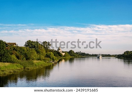 Beautiful morning landscape of the banks of the Volkhov River. In the distance is a cruise ship and a medieval fortress. Royalty-Free Stock Photo #2439191685