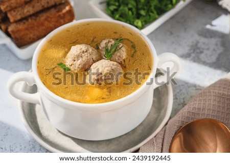 White broth bowl with handles with delicious meatball soup with croutons and herbs on a wooden background, close-up.