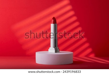 Elegant red lipstick on a white block with a cool red background.
