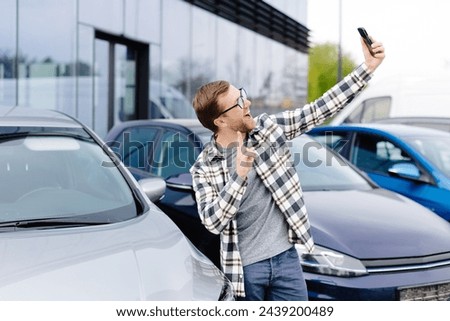 Happy man taking selfie through smart phone after purchasing new car. The man showing the purchased car via video link over the phone.