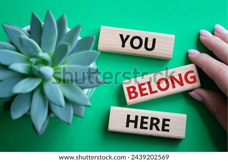 You belong here symbol. Wooden blocks with words You belong here. Beautiful green background with succulent plant. Businessman hand. Business and You belong here concept. Copy space.