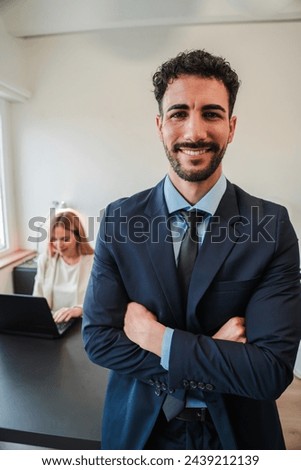 Vertical arms crossed businessman smiling and looking at camera standing at corporate office. Clerk male staring front with confident expression. Positive executive business man with suit at workplace