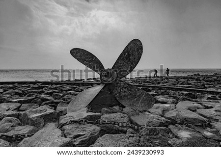 Azores, town of Povoação, name: Gate and anchor and propeller, breakwaters at the port, black and white image, in the background the propeller is raining in the foreground. A huge propeller.