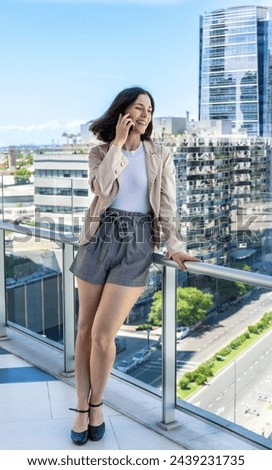 A woman is taking a break from work and chatting on her cell phone while standing on a balcony