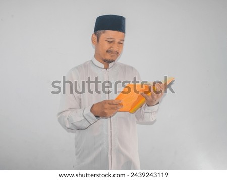 Moslem Asian man smiling at the Al Qur'an and while holding a Al-Qur'an