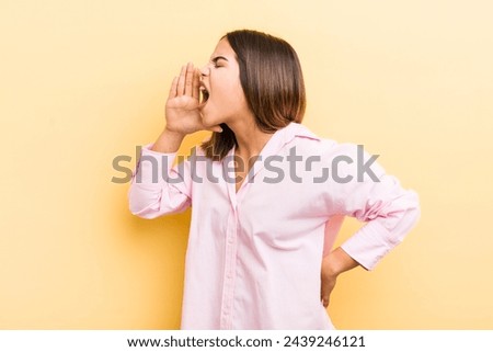 pretty hispanic woman yelling loudly and angrily to copy space on the side, with hand next to mouth