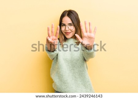pretty hispanic woman smiling and looking friendly, showing number eight or eighth with hand forward, counting down