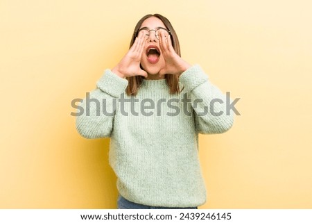 pretty hispanic woman feeling happy, excited and positive, giving a big shout out with hands next to mouth, calling out
