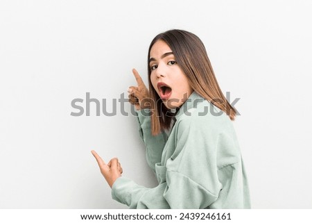 pretty hispanic woman feeling shocked and surprised, pointing to copy space on the side with amazed, open-mouthed look