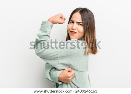pretty hispanic woman feeling happy, satisfied and powerful, flexing fit and muscular biceps, looking strong after the gym