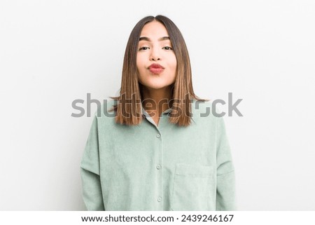 pretty hispanic woman pressing lips together with a cute, fun, happy, lovely expression, sending a kiss