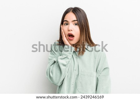 pretty hispanic woman feeling shocked and astonished holding face to hand in disbelief with mouth wide open