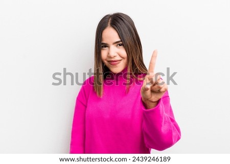 pretty hispanic woman smiling and looking friendly, showing number one or first with hand forward, counting down