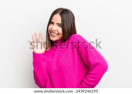 pretty hispanic woman smiling happily and cheerfully, waving hand, welcoming and greeting you, or saying goodbye