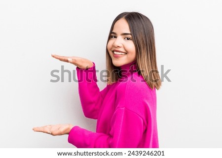 pretty hispanic woman smiling, feeling happy, positive and satisfied, holding or showing object or concept on copy space