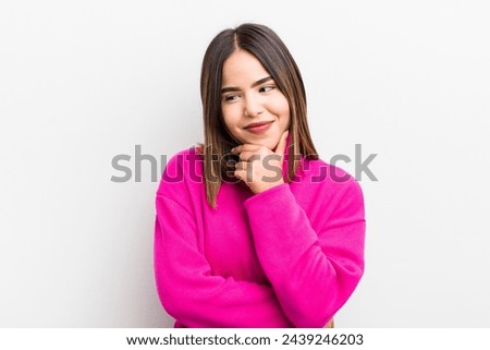 pretty hispanic woman smiling with a happy, confident expression with hand on chin, wondering and looking to the side