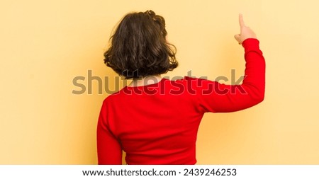 pretty hispanic woman standing and pointing to object on copy space, rear view