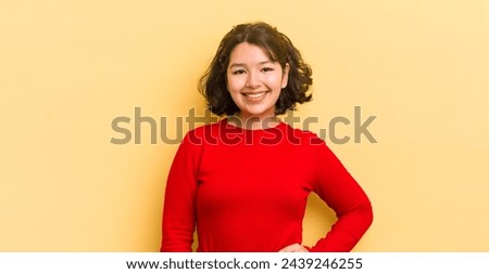 pretty hispanic woman smiling happily with a hand on hip and confident, positive, proud and friendly attitude