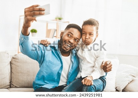 Family time. Happy afro father taking selfie with his cute daughter at home, sitting on sofa