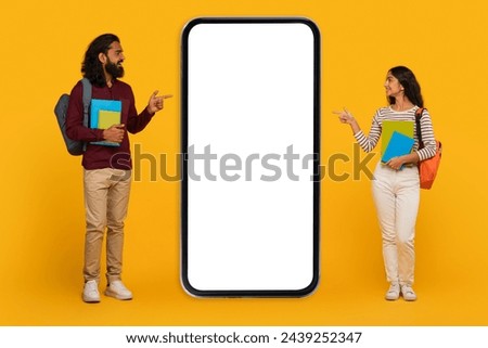 Young, trendy-dressed man and woman pointing to a blank smartphone screen mockup on a yellow background