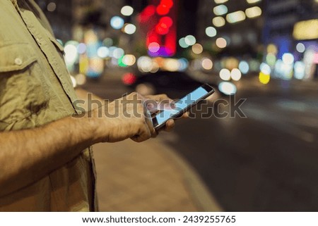Close up View of Smart Phone in Male Hand in the City Streets with Illuminated Lights in Background