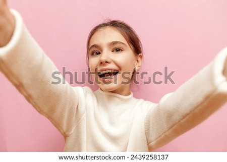 cheerful teenage girl raises her arms forward and hugs on a pink isolated background, a happy child takes a photo of herself and greets
