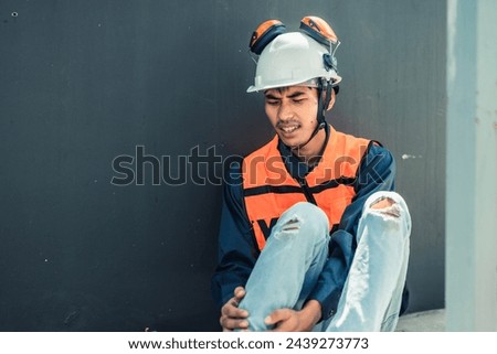 Asian HVAC engineer suffered serious leg injury on the job. Urgent first aid and assistance from coworkers is essential. Expressions of pain on face convey physical and emotional response. Royalty-Free Stock Photo #2439273773