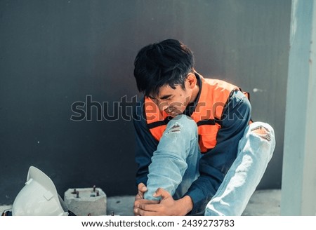 Asian HVAC engineer suffered serious leg injury on the job. Urgent first aid and assistance from coworkers is essential. Expressions of pain on face convey physical and emotional response. Royalty-Free Stock Photo #2439273783