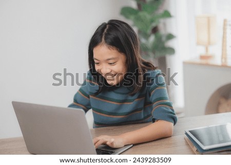 A young girl is sitting at a desk with a laptop and a tablet. She is smiling and she is enjoying her time