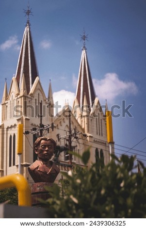 A statue of a hero with a church background in the middle of the city in the middle of the day with a clear sky 