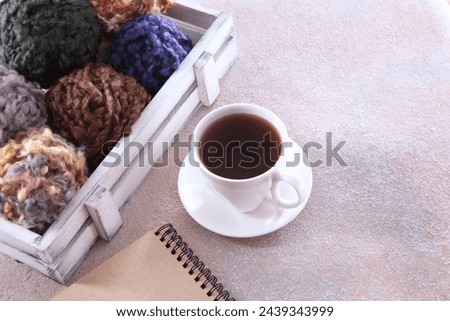 Various skeins of wool yarn in wooden box. Cup of tea . Notepad for writing. Threads for knitting handmade winter clothes. Colorful background with ball of yarn. Background for knitting.