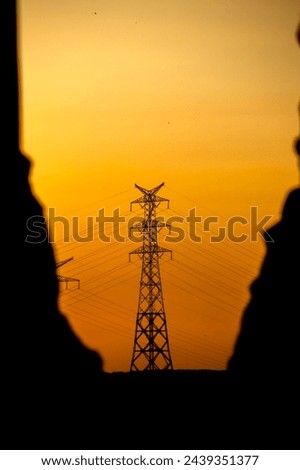 High voltage line tower. Lamppost silhouette in yellow or orange sunset colors. Energy transmission systems. Metaphorical meaning of power outage. Vertical photo. No people, nobody.