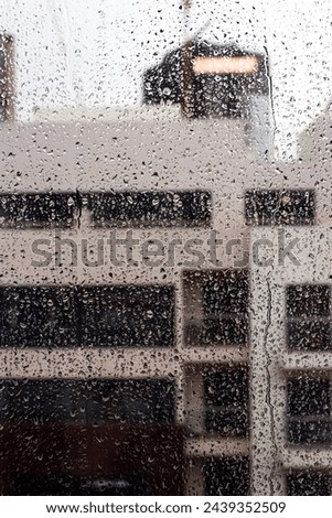 Rain drops on the window glass, grey cloudy sky and building are blurred on the background. Rainy weather concept. Close-up shot, vertical orientation