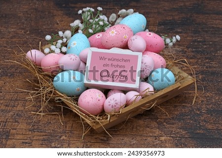 Greeting card Happy Easter: Easter basket with candy-colored Easter eggs.German inscription translated means we wish you a happy Easter.
