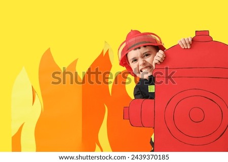 Cute little firefighter with paper hydrant and flame on yellow background