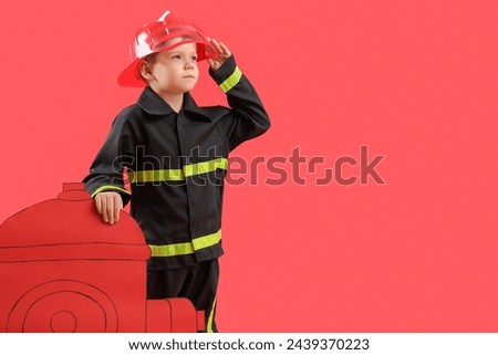 Cute little firefighter with paper hydrant on red background