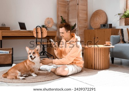 Redhead young happy man taking photo of cute Corgi dog at home