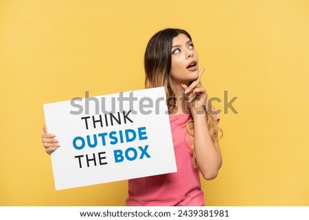 Young Russian girl isolated on yellow background holding a placard with text Think Outside The Box and thinking