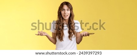 Pissed frustrated bothered curly-haired caucasian girl stare camera puzzled complain hold smartphone shrugging spread hands sideways dismay arguing after intense serious phonecall yellow background. Royalty-Free Stock Photo #2439397293