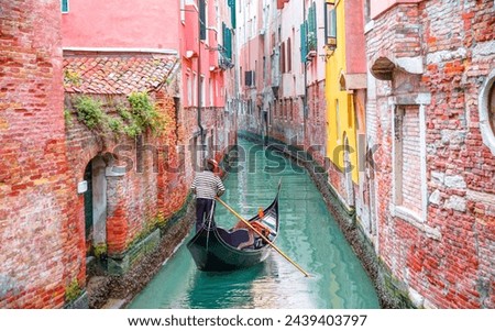 Venetian gondolier punting gondola through green canal waters of Venice Italy Royalty-Free Stock Photo #2439403797