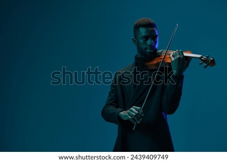 Elegant man in suit playing classical violin music on blue background in professional music studio