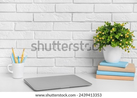 Stylish workplace with laptop and houseplant near white brick wall