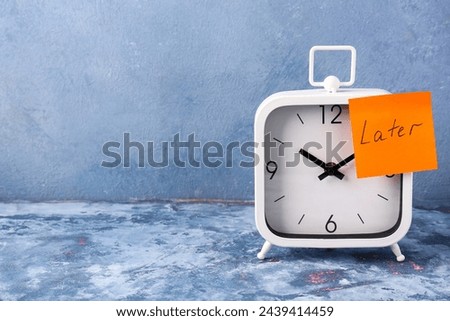 Text LATER with white alarm clock on table against blue background. Time management