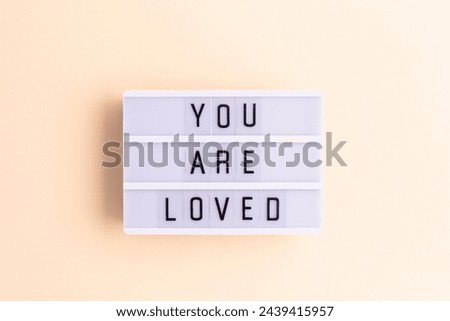 You are loved. White lightbox with letters on a beige background. 