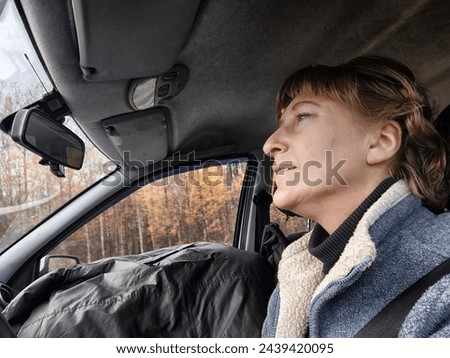 Funny cute blonde girl or a middle-aged woman driving a car in summer, autumn, spring day. A female driver on a solo trip