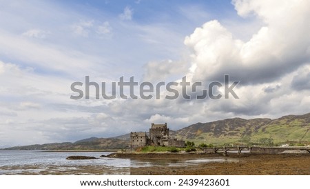 Eilean Donan Castle, a historic Scottish fortress, stands on a loch's islet under a vast sky, with a bridge arching towards the wild Highlands Royalty-Free Stock Photo #2439423601