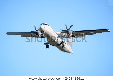 ATR 72 airplane, a twin-engine turboprop short-haul regional passenger aircraft. Landing airplane. Blue background. Clear sky. Royalty-Free Stock Photo #2439436611