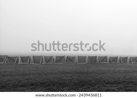 Wooden barriers in a fogged landscape, wooden barriers between the road and the field, black and white photo