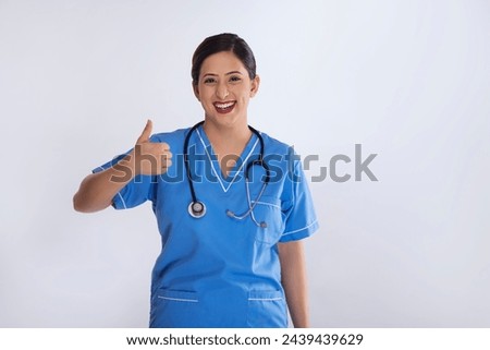 Portrait of smiling female nurse showing thumbs up sign against white background Royalty-Free Stock Photo #2439439629