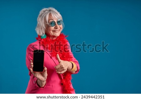 Tech-savvy senior showcasing smartphone and doing thumbs up Royalty-Free Stock Photo #2439442351